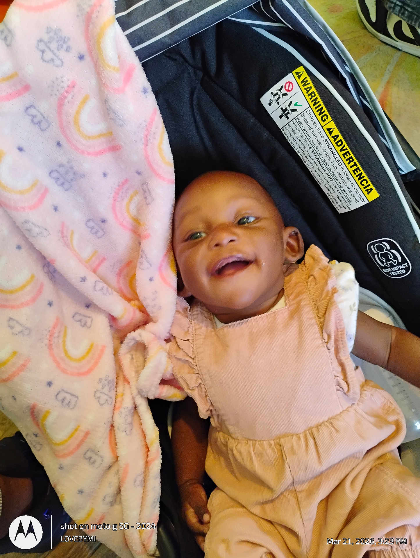 Evvie is registered to the contest to win money with this photo: baby, smiling, infant, car_seat, blanket, pink_blanket, onesie, ruffle_dress, happy, face, hand, safety_label, warning_label, strap, stroller, shoe, floor, timestamp, watermark, portrait