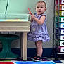 toddler, child, purple_dress, marker, table, classroom, colorful, art_supplies, shoes, floor, wall, storage_drawers, toy, standing, indoor, person, young_child, play, learning, education
