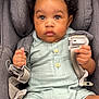 baby, child, car_seat, curly_hair, harness, pastel_clothing, green_outfit, buttons, infant, seatbelt, sitting, cute, portrait, indoors, young_child, grip, looking_at_camera, serious_expression, soft_fabric, toddler