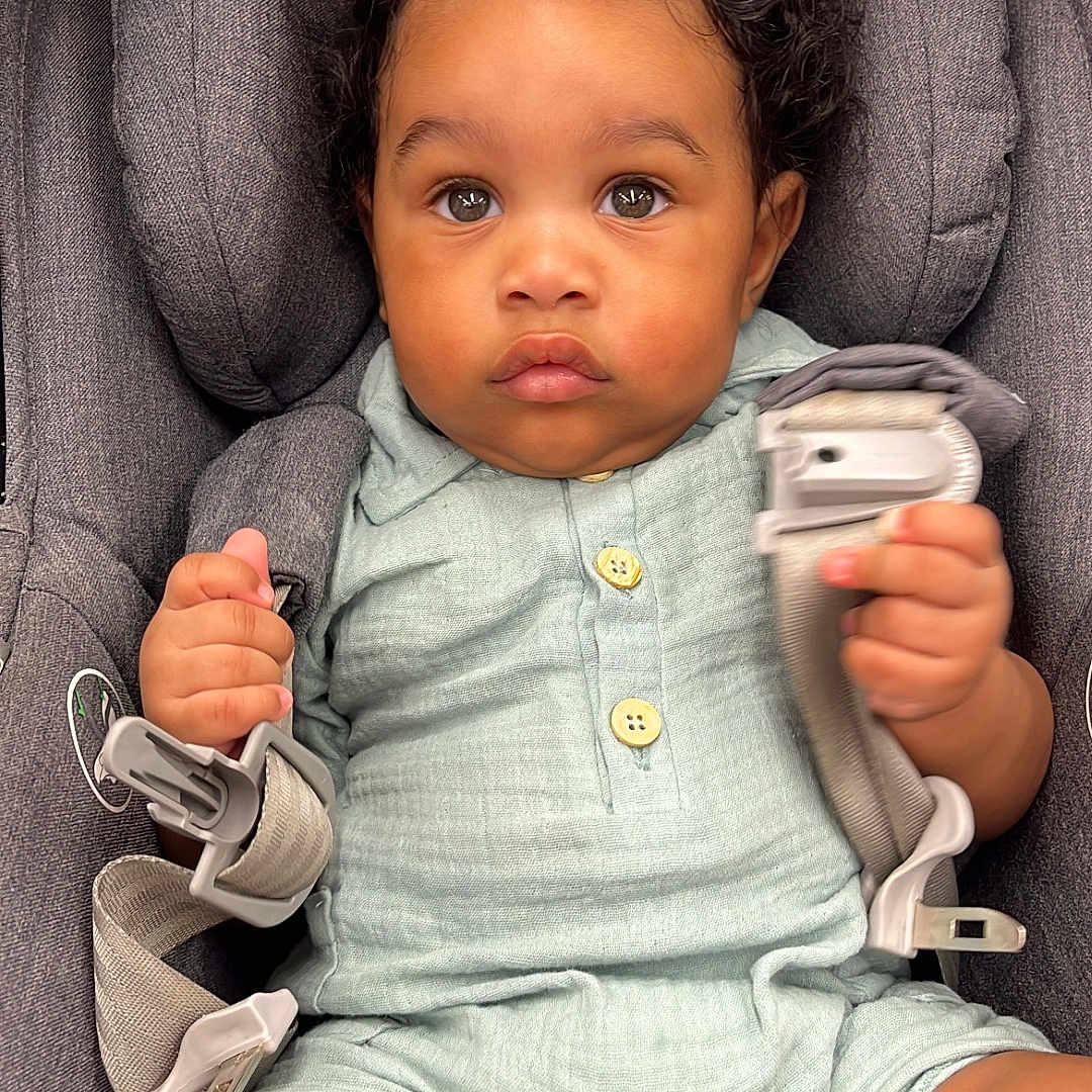 Nolan joined the competition — help win amazing prizes! baby, buttons, car_seat, child, curly_hair, cute, green_outfit, grip, harness, indoors, infant, looking_at_camera, pastel_clothing, portrait, seatbelt, serious_expression, sitting, soft_fabric, toddler, young_child