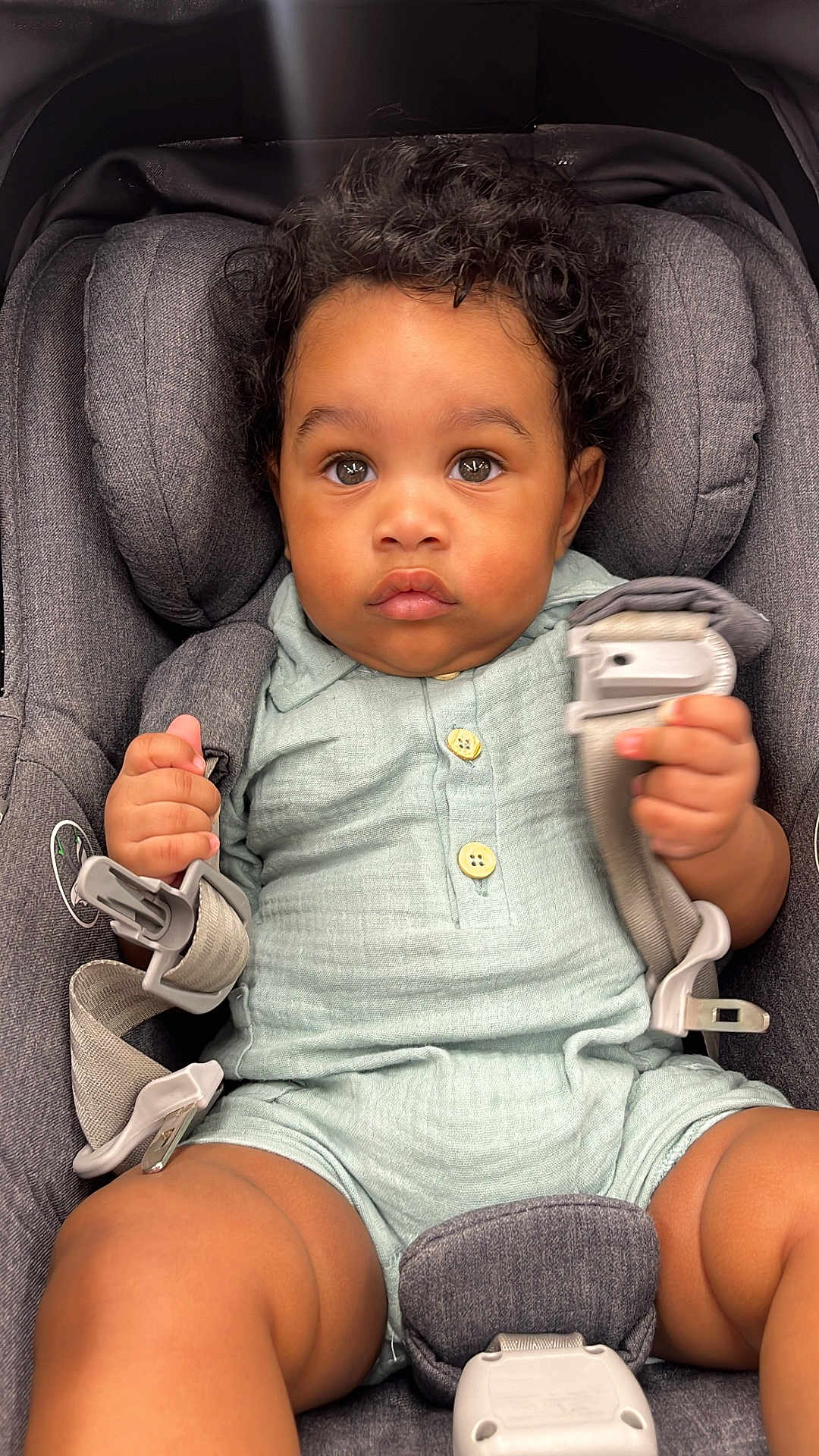 Nolan joined the competition — help win amazing prizes! baby, child, car_seat, curly_hair, harness, pastel_clothing, green_outfit, buttons, infant, seatbelt, sitting, cute, portrait, indoors, young_child, grip, looking_at_camera, serious_expression, soft_fabric, toddler
