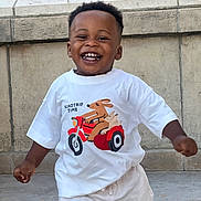 Nathan a rejoint le concours — aidez-le/la à gagner de superbes lots ! toddler, child, smiling, happy, white_tshirt, graphic_tee, shorts, outdoor, stone_wall, motion, playful, cute, young_child, portrait, casual_clothing, daylight, person, joy, expression, fun