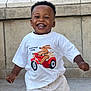 toddler, child, smiling, happy, white_tshirt, graphic_tee, shorts, outdoor, stone_wall, motion, playful, cute, young_child, portrait, casual_clothing, daylight, person, joy, expression, fun