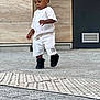 Nathan participe au concours pour gagner de l'argent avec cette photo : toddler, child, walking, white_clothing, black_shoes, outdoor, concrete, urban, door, wall, vent, shorts, tshirt, person, young_child, curly_hair, side_view, casual, daylight, focused