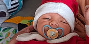 Tyler participe au concours pour gagner de l'argent avec cette photo : baby, infant, santa_hat, red_clothing, pacifier, indoor, holiday_outfit, cute, sleepy, person, child, festive, christmas, smile, hand, face, headwear, blanket, couch, comfort