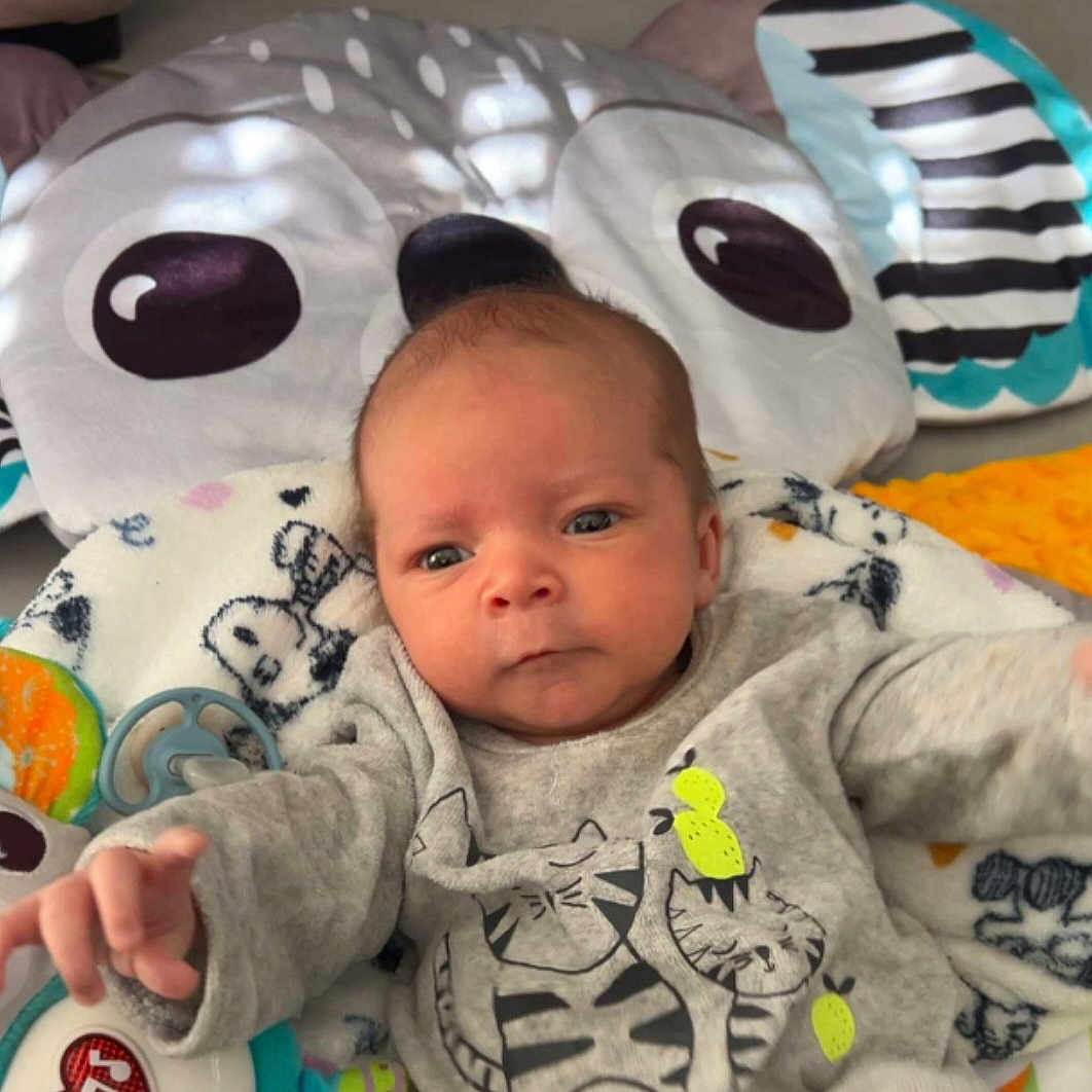 Tyler participe au concours pour gagner de l'argent avec cette photo : baby, blanket, child, clothing, cute, expression, face, floor, gray_sweater, hand, indoor, infant, lying_down, owl, pattern, person, pillow, play_mat, toy, young