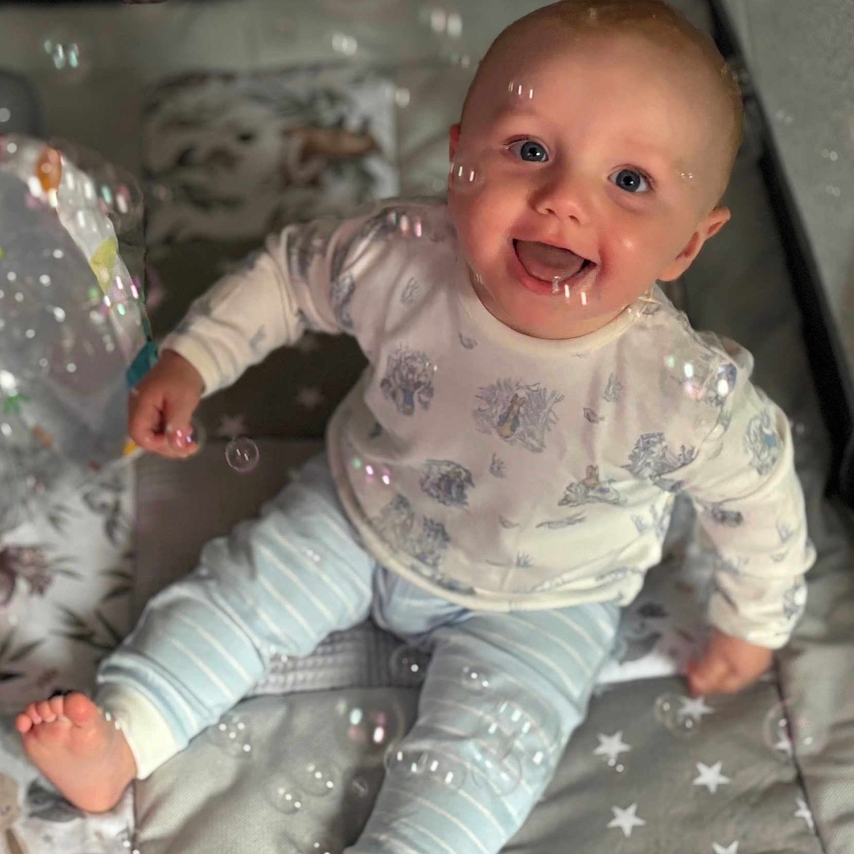 Asher is registered to the contest to win money with this photo: baby, barefoot, blue_eyes, bubbles, child, close_up, clothing, cute, face, happy, indoor, infant, joyful, patterned_shirt, play_mat, portrait, sitting, smiling, soft_lighting, striped_pants