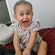 Kehlani joined the competition — help win amazing prizes! baby, child, smiling, happy, curly_hair, floral_dress, tablet, indoor, bed, sitting, hands, face, joyful, cute, person, room, sneaker, power_outlet, casual, home