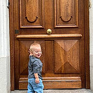 Abel a rejoint le concours — aidez-le/la à gagner de superbes lots ! toddler, child, smiling, standing, jeans, sneakers, wooden_door, door, outdoor, happy, casual_clothing, blonde_hair, laughing, concrete, sidewalk, urban, young_child, person, candid, daylight