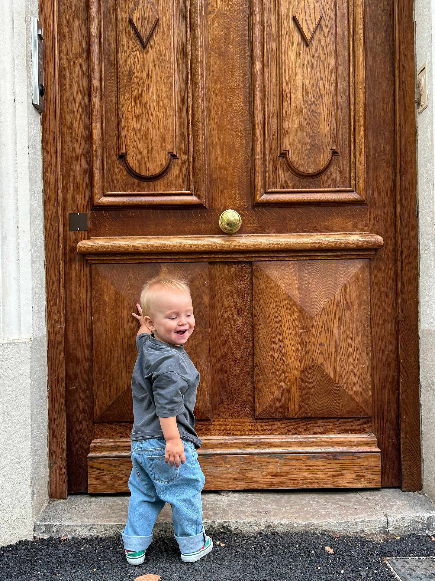 Abel a rejoint le concours — aidez-le/la à gagner de superbes lots ! toddler, child, smiling, standing, jeans, sneakers, wooden_door, door, outdoor, happy, casual_clothing, blonde_hair, laughing, concrete, sidewalk, urban, young_child, person, candid, daylight