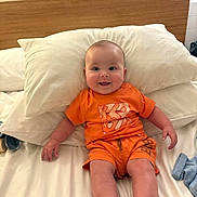 Theo joined the competition — help win amazing prizes! baby, infant, smiling, orange_clothing, bed, pillow, wooden_headboard, white_bed_sheet, happy, child, indoors, cute, human, portrait, one_person, sitting, young_child, casual, relaxed, comfortable