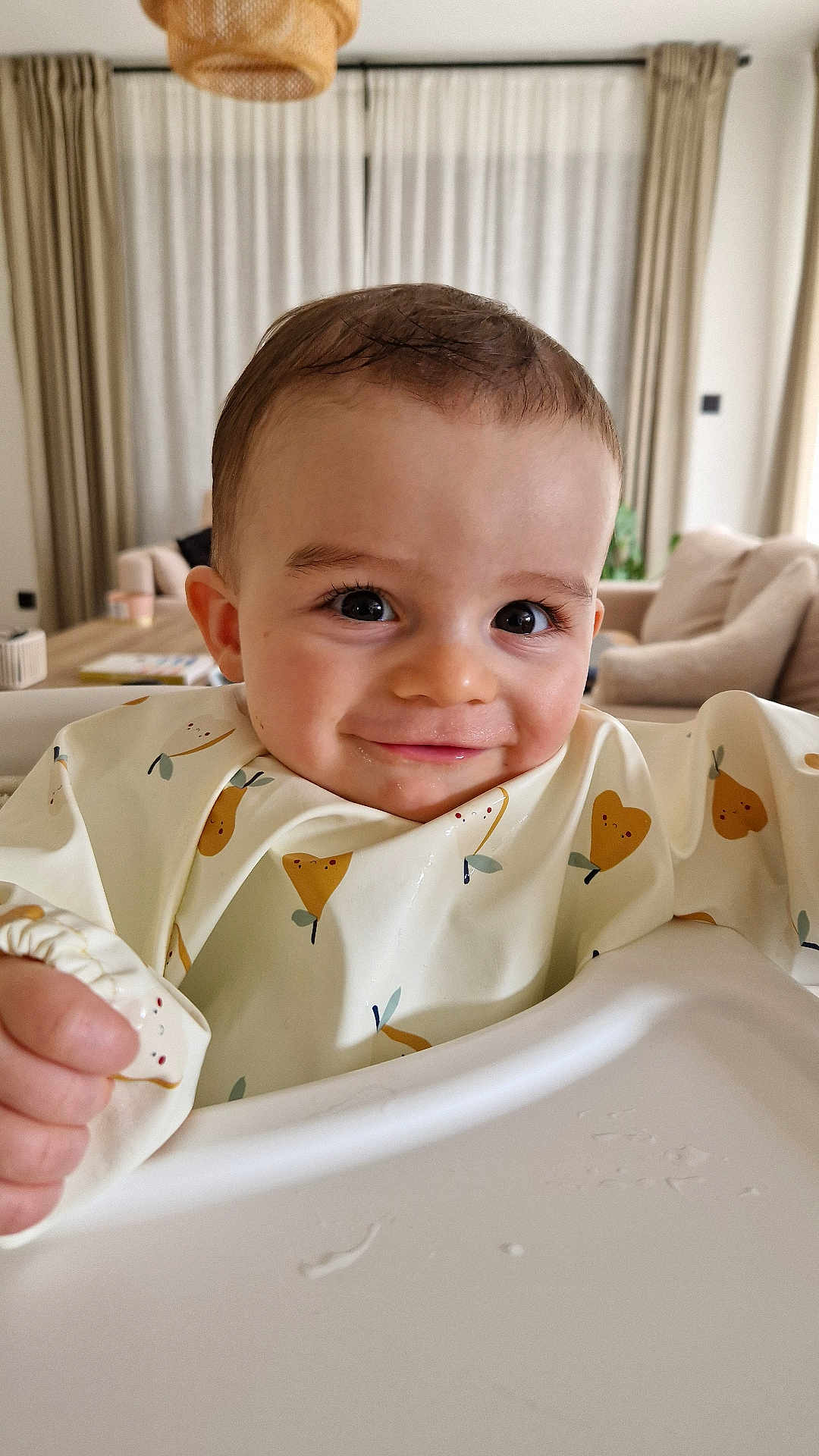 Milo a rejoint le concours — aidez-le/la à gagner de superbes lots ! baby, child, smiling, high_chair, bib, indoor, living_room, curtains, sofa, table, furniture, cute, portrait, face, happy, young, clothing, infant, human, home