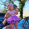 baby, child, purple_tutu, headband, smiling, outdoor, car, tree, hand, supporting, sunny, blue_sky, reflection, person, clothing, cute, happy, infant, nature, portrait