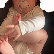 Kyla is registered to the contest to win money with this photo: baby, infant, pacifier, white_clothing, diaper, barefoot, hand, foot, cute, child, lying_down, skin, face, expression, playful, indoors, soft_light, close_up, person, newborn
