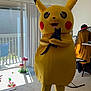pikachu_costume, person, black_cat, indoor, living_room, carpet, vertical_blinds, sunlight, cat_toys, chair, hat, clothing, table, window, door, furniture, playful, animal, costume, pet
