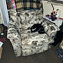 cat, tuxedo_cat, recliner, armchair, blanket, patterned_fabric, bookshelf, toy_truck, cat_tree, blinds, carpet, indoor, sleeping, cozy, living_room, pillow, flash_photo, paw, decor, shelf