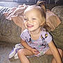 toddler, child, smiling, indoor, couch, blanket, shorts, shirt, happy, person, hair, pony_tail, patterned_fabric, sitting, young_child, casual_clothing, home, playful, joyful, blurry