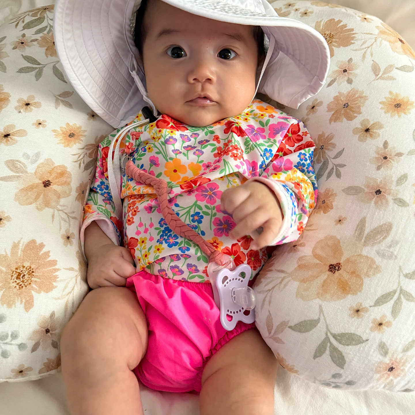 Viveeana is registered to the contest to win money with this photo: baby, child, closeup, colorful_clothing, cute, face, floral, hat, indoors, infant, pacifier, person, pillow, pink, relaxing, sitting, skin, soft_fabric, white, young