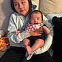 child, baby, couch, hugging, smiling, plush_toy, giraffe, hoodie, bib, family, indoor, comfort, sibling, casual_clothing, happy, seated, portrait, human, relaxing, living_room