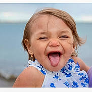 Kya joined the competition — help win amazing prizes! child, girl, tongue_out, smiling, blue_flower_dress, earrings, outdoor, water, sea, shore, playful, happy, portrait, person, summer, casual_clothing, cute, fun, face, hair