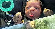 Omari joined the competition — help win amazing prizes! baby, infant, child, car_seat, portrait, face, tongue, sticking_out_tongue, looking_at_camera, serious_expression, blanket, mittens, winter_clothing, toy, teether, vehicle, seated, close_up, indoor, safe