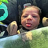 baby, infant, child, car_seat, portrait, face, tongue, sticking_out_tongue, looking_at_camera, serious_expression, blanket, mittens, winter_clothing, toy, teether, vehicle, seated, close_up, indoor, safe