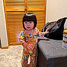 Esther Pham is registered to the contest to win money with this photo: toddler, child, pajamas, barefoot, carpet, ottoman, black_bag, infant_formula, wooden_closet, indoor, wall, floor, person, standing, curious, colorful_clothing, short_hair, home, furniture, toyless