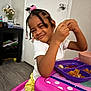 Amara joined the competition — help win amazing prizes! child, girl, braided_hair, beads, pink_beads, white_shirt, yellow_pants, table, purple_plate, food, indoor, door, doorknob, floor, flowers, shelf, plastic_table, smile, happy, meal