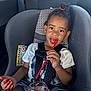 child, car_seat, drink, straw, red_drink, toddler, hair_tie, white_shirt, sitting, car_interior, seatbelt, warning_label, happy, smiling, fingers, shorts, black_hair, eating, portrait, young