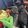 child, waiting_area, airport_chairs, casual_clothing, green_pants, yellow_shirt, black_bag, prime_label, seated_person, resting, indoor, metal_armrest, white_shoes, thoughtful, waiting, public_space, travel, luggage, relaxed, people