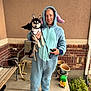 bat_wings, bench, brick_wall, concrete_floor, costume, cute, dog, halloween, leash, onesie, outdoor, person, pet, plant_food, plant_pots, porch, red_shoes, skeleton_dog, smiling, sweater