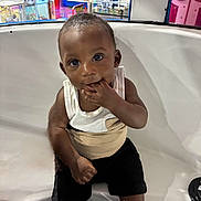 Jaylen joined the competition — help win amazing prizes! baby, toddler, child, sitting, playing, hand_in_mouth, white_tank_top, black_shorts, sneakers, arcade, colorful_background, indoor, play_area, smiling, cute, curious, face, person, seat, fun