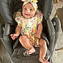 baby, child, smiling, infant, headband, floral_dress, baby_seat, gray_seat, happy, cute, indoors, person, legs, feet, arm, skin, seat_belt, comfort, joy, portrait