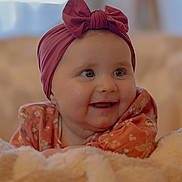 Zélie participe au concours pour gagner de l'argent avec cette photo : baby, blanket, bow, child, closeup, cozy, cute, expression, face, floral_clothing, happy, headband, indoors, infant, person, portrait, smiling, soft_light, toddler, warm_colors