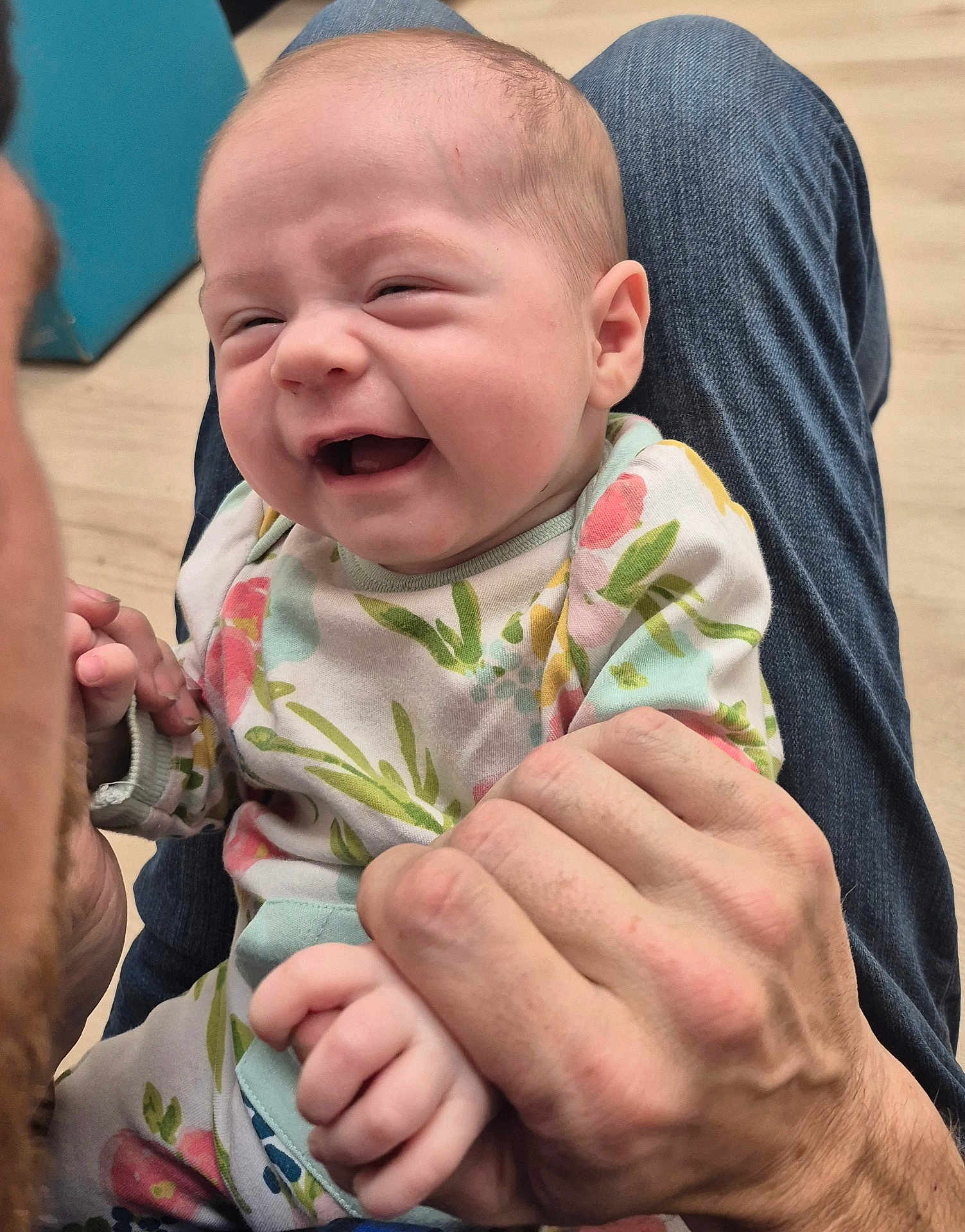 Phoenix is registered to the contest to win money with this photo: baby, infant, smiling, laughing, hands, holding, floral_clothing, pajamas, denim, floor, joy, happy, person, skin, face, head, cute, playful, closeup, indoors