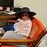 Rhyli joined the competition — help win amazing prizes! carpet, casual, chair, child, computer_monitor, desk, fashion, hat, indoor, office, orange_chair, person, pink_coat, portrait, printer, relaxed, shoe, socks, wooden_armrest, young_kid