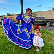 Kassandra is registered to the contest to win money with this photo: child, children, girl, toddler, traditional_clothing, dress, blue_dress, white_dress, flower_headband, grass, outdoor, daylight, car, building, smile, holding_hands, posing, happy, nature, cultural