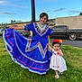 child, children, girl, toddler, traditional_clothing, dress, blue_dress, white_dress, flower_headband, grass, outdoor, daylight, car, building, smile, holding_hands, posing, happy, nature, cultural