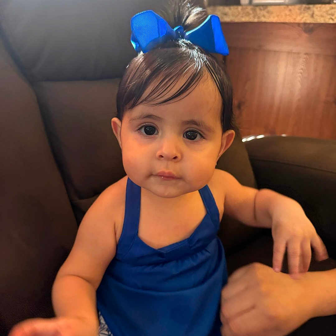 Kassandra joined the competition — help win amazing prizes! baby, blue_bow, blue_dress, chair, child, cute, expression, face, furniture, hair, hands, human, indoor, patterned_pants, person, portrait, sitting, skin, toddler, young_child