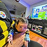 baby, infant, child, face, eyes, wide_eyed, indoor, living_room, family_room, adult, holding, football, television, sports, sofa, clock, chandelier, wood_floor, portrait, home