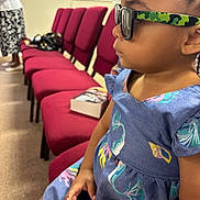 Jenasis joined the competition — help win amazing prizes! child, girl, sunglasses, blue_dress, seated, indoor, red_chairs, book, hand, profile, fashion, patterned_dress, person, room, carpet, window_ac, casual, accessory, serious, waiting