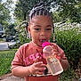 Jenasis joined the competition — help win amazing prizes! toddler, child, water_bottle, beads, braided_hair, outdoor, flowers, greenery, grass, sidewalk, smiling, happy, person, nature, daylight, cute, casual_clothing, pink, shirt, neighborhood