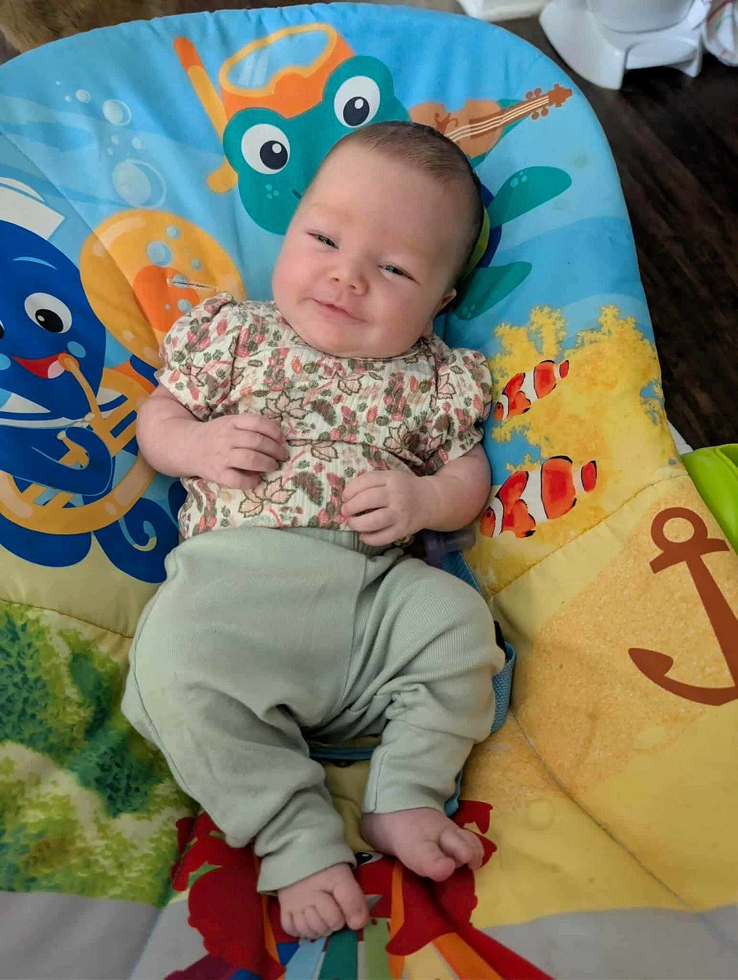Aurelia is registered to the contest to win money with this photo: baby, infant, smile, face, person, cushion, colorful, underwater_theme, cartoon, sea_creatures, octopus, fish, anchor, floor, clothing, pants, shirt, happy, relaxing, indoor