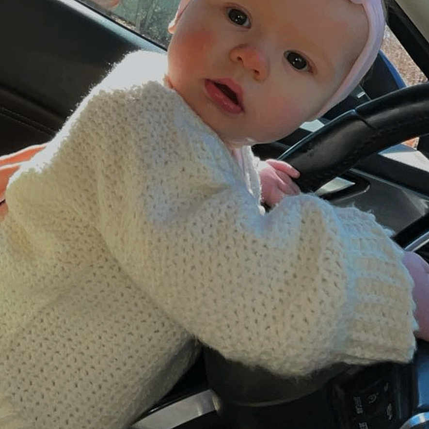 Adalin joined the competition — help win amazing prizes! baby, bonnet, cap, clothing, coat, face, glove, hat, head, hood, jacket, knitwear, person, photography, portrait, sitting, steeringwheel, sweater, transportation, vehicle