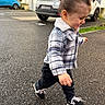 toddler, child, plaid_jacket, black_pants, sneakers, walking, outdoor, asphalt, car, residential_building, happy, side_view, curly_hair, street, urban, daylight, casual_clothing, smiling, young_child, playful