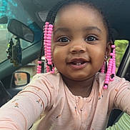 Barbie is registered to the contest to win money with this photo: child, toddler, smiling, braids, pink_beads, face, eyes, clothing, long_sleeves, car_interior, seat, mirror, window, door, person, portrait, cute, happy, young_child, indoors