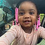 child, toddler, smiling, braids, pink_beads, face, eyes, clothing, long_sleeves, car_interior, seat, mirror, window, door, person, portrait, cute, happy, young_child, indoors