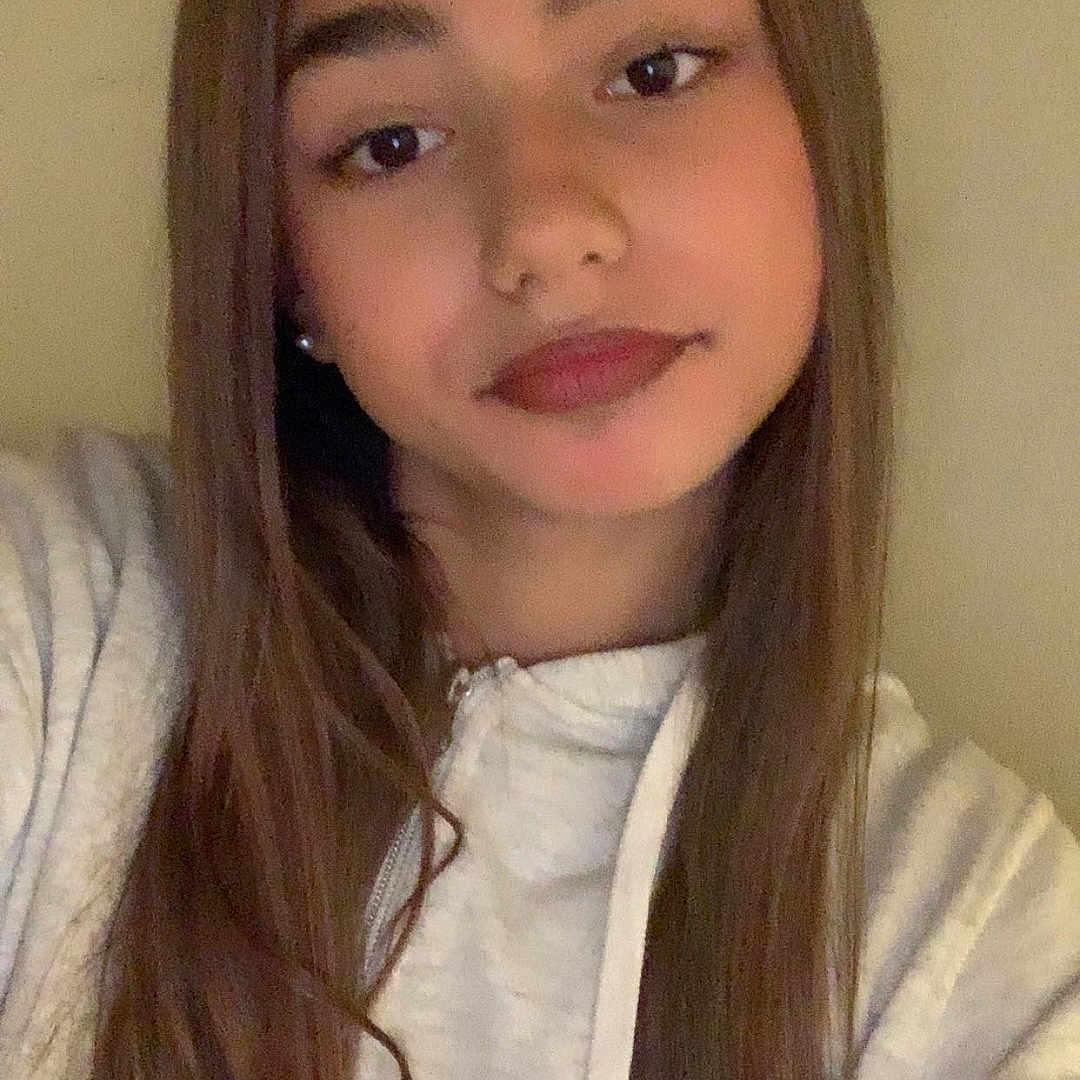 Tanya a rejoint le concours — aidez-le/la à gagner de superbes lots ! brown_hair, casual_clothing, child, closeup, earrings, eyebrows, eyes, face, hoodie, indoor, lips, long_hair, neutral_expression, portrait, selfie, shoulder, smile, straight_hair, wall, young_person