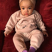 Nova joined the competition — help win amazing prizes! baby, child, pajamas, headband, bow, socks, purple_socks, couch, red_couch, plush, indoor, portrait, cute, cozy, clothing, person, seated, looking_at_camera, face, infant