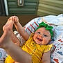 baby, child, smiling, yellow_clothing, green_headband, blue_eyes, infant, happy, playful, cushion, patterned_fabric, indoor, cute, cheerful, skin, person, one_piece, headwear, small_child, baby_toys